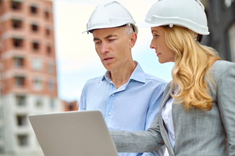 question profile demanding business woman with long blond hair protective helmet looking attentively talking man with laptop standing construction site